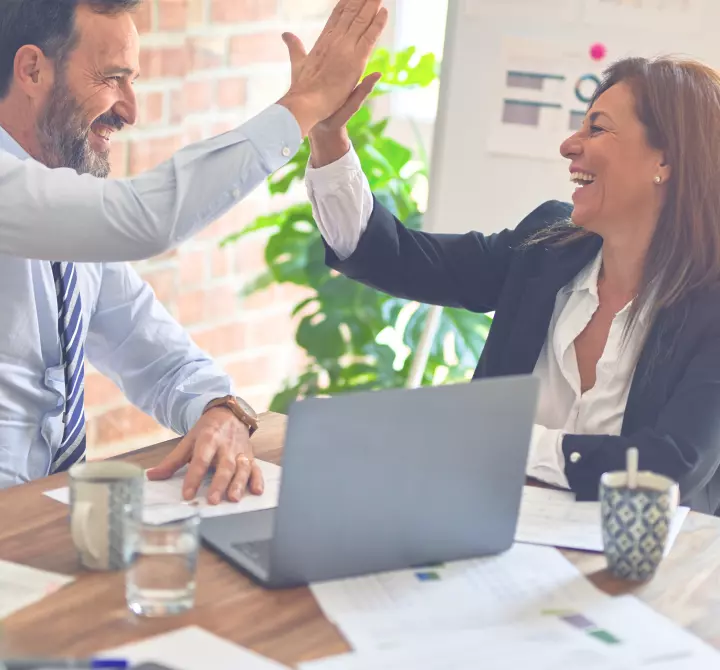 Two people celebrating a completed transaction across a work table.